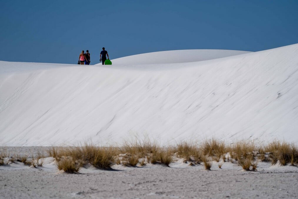 ourists hike with sleds on the gypsum sand dunes to go sledding in White Sands National Park